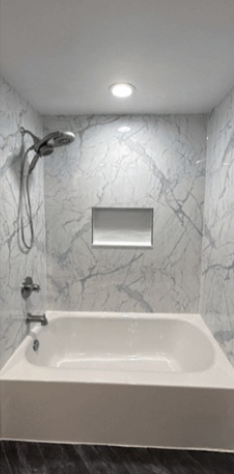 Bathroom after remodel: new tub with marble-look wall panels and niche